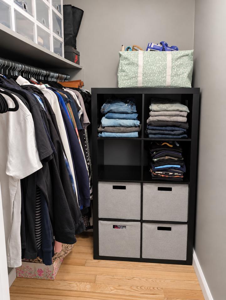Closet after organizing, with folded clothing on shelves, fabric drawers and a clear floor