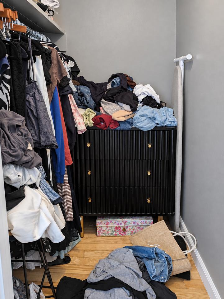 Closet before organizing, with clothing piled on a cabinet and across the floor
